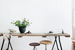 Bouquet (Nigella) in black ceramic vase on rustic wooden tabletop on metal trestles, partially visible vintage swivel stools under table