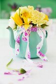 Yellow spring posy of tulips, carnations and narcissus in turquoise teapot