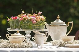 Romantisch elegant gedeckter Kaffee-Gartentisch mit Blumendekoration auf Glas-Tortenplatte und zarten Schleierkraut- Kränzen