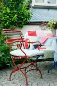 Vintage-Gartenstuhl auf Kopfsteinpflaster-Terrasse und gemütlicher Bank mit Patchworkdecke