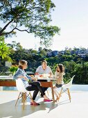 Family sitting on classic chairs at designer table on sunny terrace