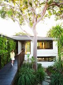 Girl on wooden bridge leading to upper storey of renovate, two-storey 60s house