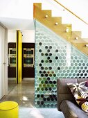 Storage space below stairs behind glass wall with honeycomb wine rack