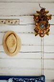 Straw hat next to cuckoo clock on white wooden wall