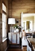 Lamp with demijohn base on vintage cabinet against unrendered clay wall in dining room