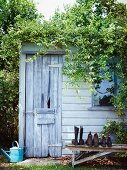 Garden shed with rustic wooden door and shoes on weathered wooden bench