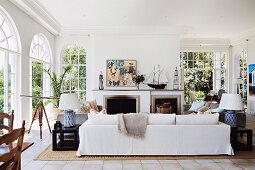 White sofa in front of open fireplace in elegant, traditional living room with arched French windows