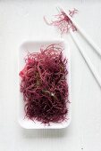 A bowl of red seaweed with chopsticks