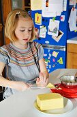 A girl in a kitchen cutting a piece of butter