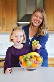 A mother and daughter in the kitchen with a bowl of fruit