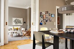 Black dining table below glossy pendant lamp in pale grey dining room with view into living room through open sliding door