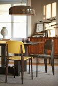 Modern dining table and chairs below glossy pendant lamp in sunny dining room with grey walls