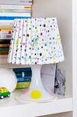 Table lamp with confetti-patterned lampshade on bookshelf