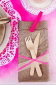 Linen napkin and wooden cutlery on place mat sprayed hot pink through doily stencils