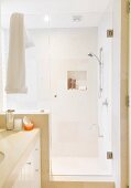 Shower area with glass door and sand-coloured wall tiles in modern bathroom