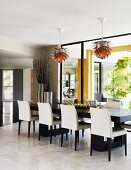 Elegant black and white dining chairs around long table below Bauhaus pendant lamps next to glass wall