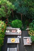 View down onto wooden deck with modern table and sofa set in densely planted garden