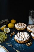 Lemon meringue pies, fresh lemons, icing sugar and a spoon