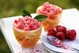 Raspberry granita with mint and fresh raspberries in orange glass bowls