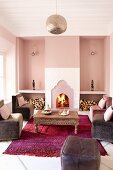 Armchairs around coffee table on magenta rug in front of open fireplace flanked by stacked firewood in elegant ambiance