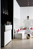 Counter and pendant lamps next to open-plan, minimalist lounge area with white, upholstered bench and metal stool