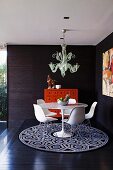 Round dining room with shell chairs, rug & postmodern ceiling lamp on platform in corner of room with dark wood panelling