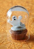 A cupcake decorated with a ghost for Halloween under a glass cloche