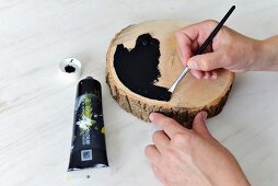 Bemalen einer Holzscheibe mit Pinsel und schwarzer Farbe