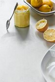 A jar of lemon cream with a spoon and a bowl of fresh lemons next to it