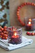 Lit candle in tealight holder with painted pattern in front of rose hip posy and rose hip wreath