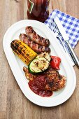 Barbecued food on an oval platter (pork steak, sausages and grilled vegetables)