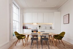 Simple, white fitted kitchen in renovated period apartment with lattice window, wooden floor and retro-style dining area