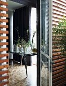 View through terrace doors into interior; various glass vases and plant stems on table