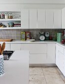 Corner of counter in fitted kitchen with white cabinet doors and sand-coloured stone floor