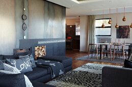 Offenes Wohnen im Designerstil - Sofakombination im Loungebereich mit Teppich, moderner offener Kamin mit Metallverkleidung im Hintergrund Essplatz
