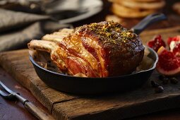 Roast pork roast in an iron pan on a wooden board with a pomegranate blood oranges