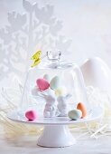 Colourful Easter eggs and Easter bunnies under a glass cloche