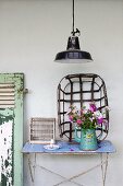 Bouquet in vintage enamel coffee pot on old garden table and metal basket leaning against white wall