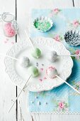 Fünf verschiedene Cake Pops auf Teller mit Zuckerperlen im Hintergrund