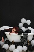 Frau liegt erschöpft in mit Luftballons gefüllter Badewanne