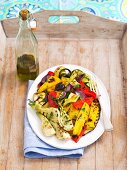 A plate of grilled vegetables and a bottle of olive oil on a wooden tray