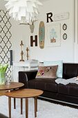 Set of 50s-style side table in front of black leather sofa, ogee-patterned wallpaper and vintage ornaments in background