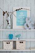 Framed motto, ornaments and white-painted wicker baskets on floating shelves on exposed concrete wall