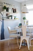 Dining area with white retro furniture, glasses and vintage ornaments on shelves against tree trunk silhouette mural