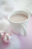 A cup of hot chocolate between feathers and Christmas baubles