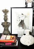 Vase with three-dimensional floral details, stacked books, antique metal candlestick and framed drawing of woman on cabinet