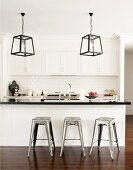 Lantern-style lamps and industrial-look metal stools at breakfast bar in black and white fitted kitchen
