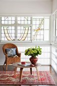 Vase of flowers on low, 50s-style side table and wicker chair in front of window with art nouveau glazing