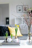 Spring atmosphere in living room - spring flowers in small containers and flowering branches in glass vase