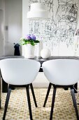 Retro, white shell chairs with black frames around table in front of black and white drawing on wall